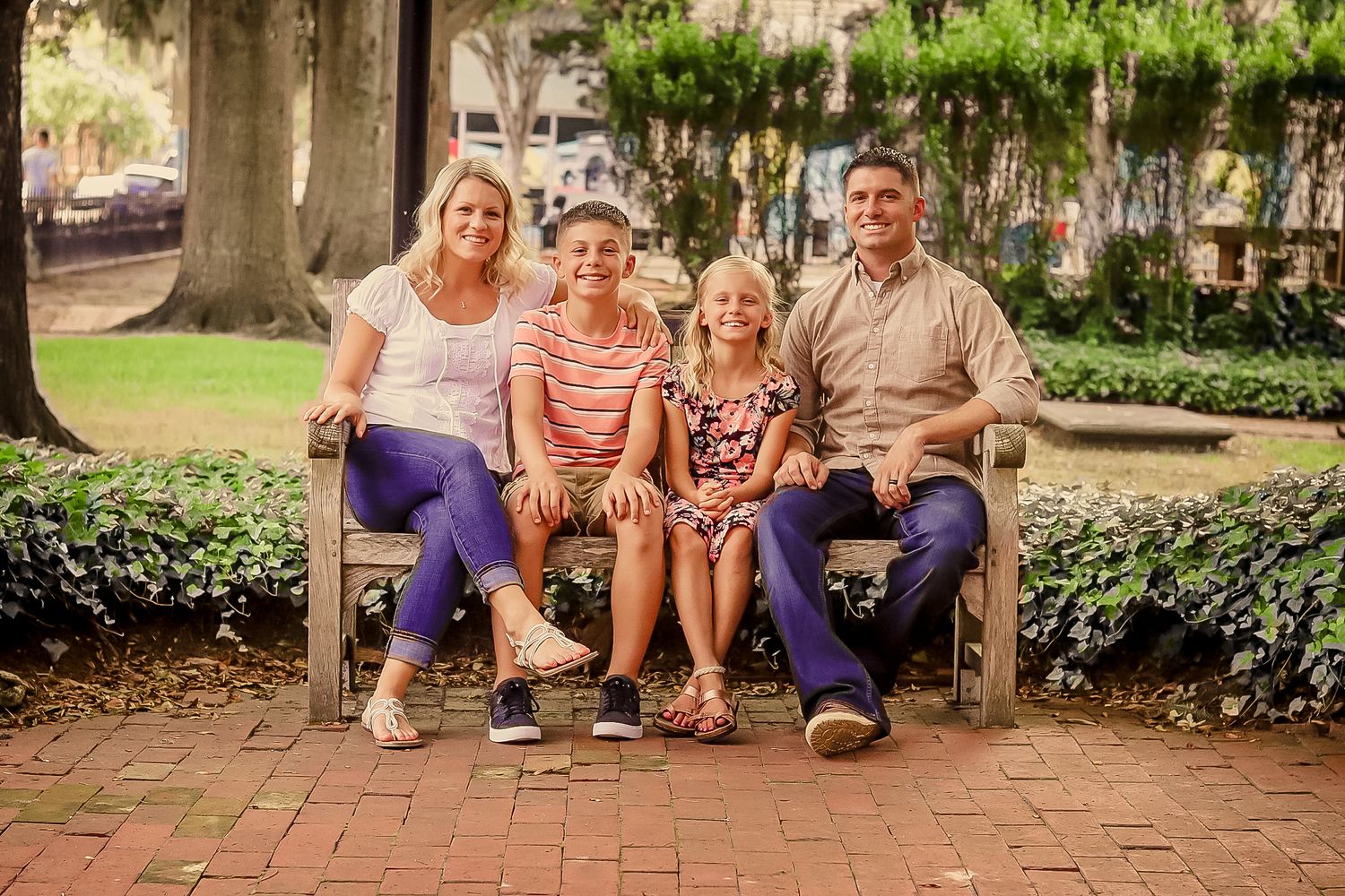 Family of four smiling together on a bench in a lush park setting.