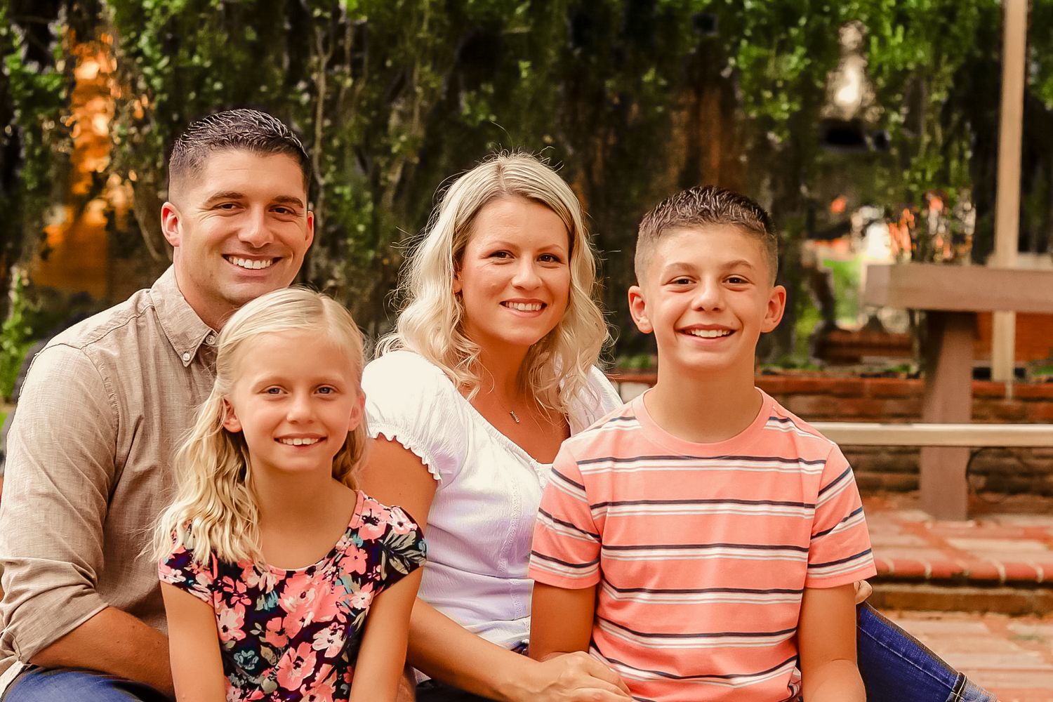 Smiling family of four posing together outdoors in a garden setting.