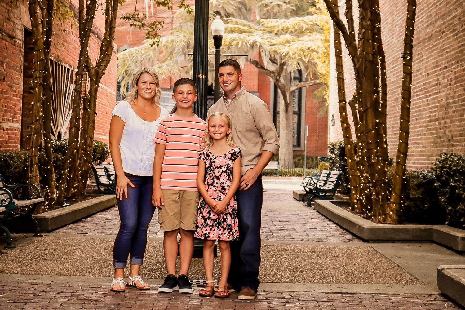 Happy family of four posing in a charming brick alleyway with twinkling lights.