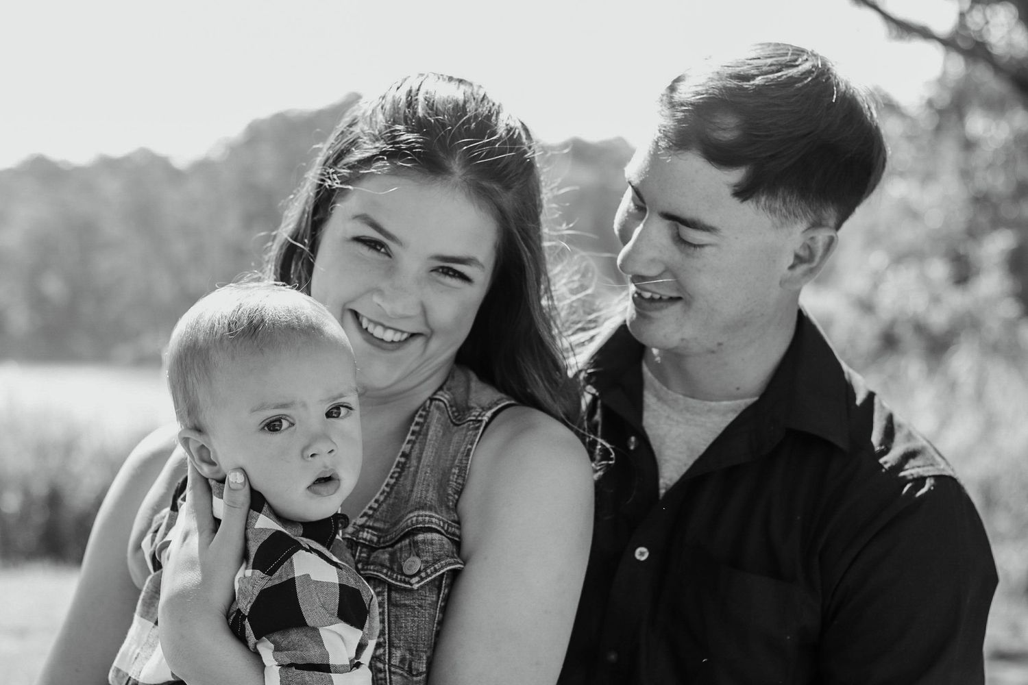 Black and white photo of smiling couple holding baby outdoors.