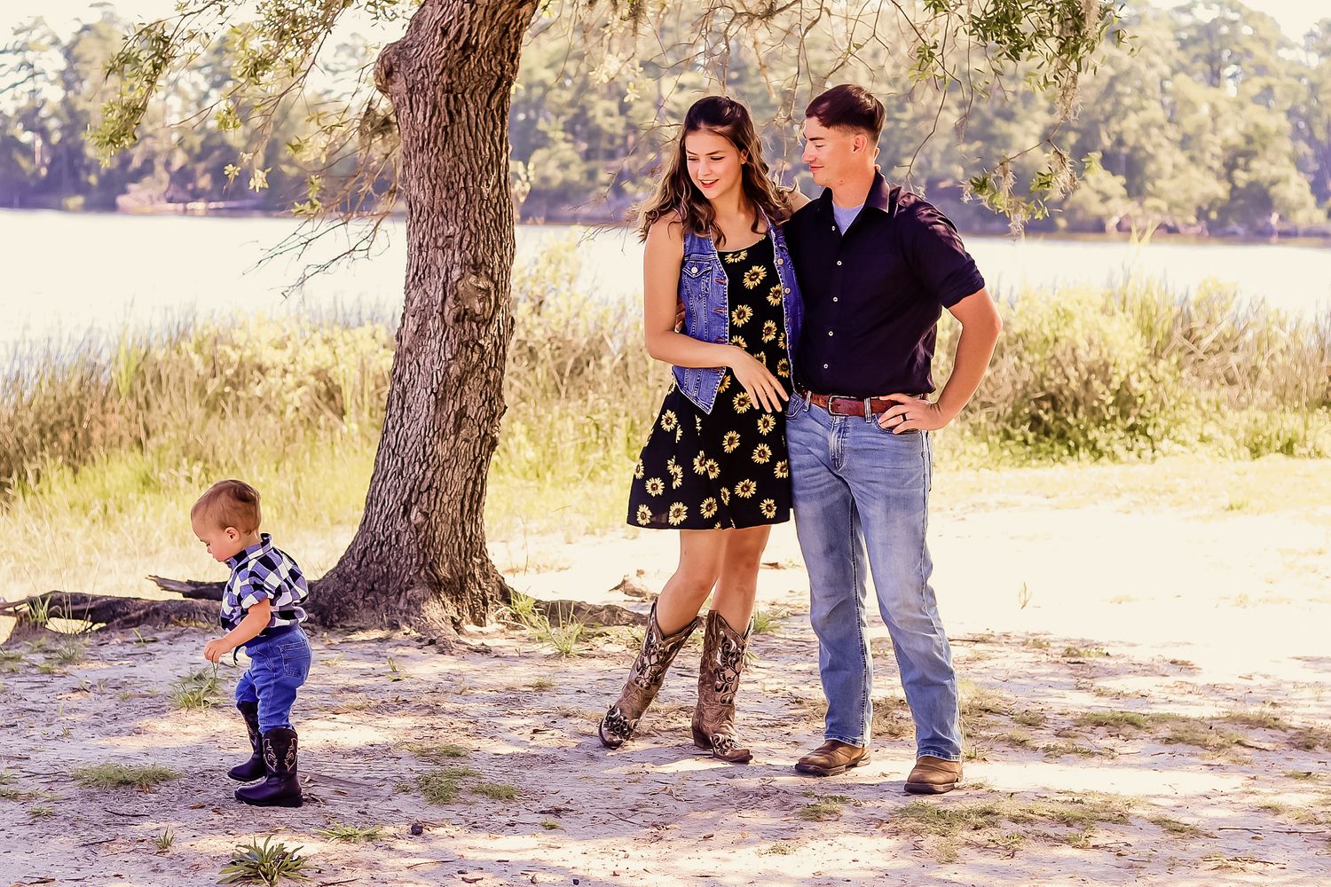 Young family with toddler enjoying an outdoor photo session near a tree by a lake.