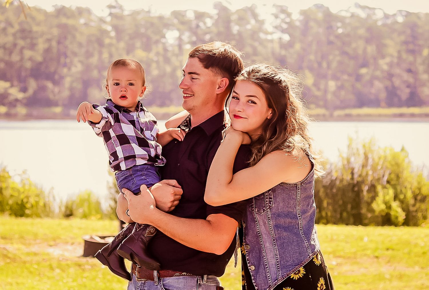 Happy family with mother, father, and baby boy posing together outdoors by a lake.