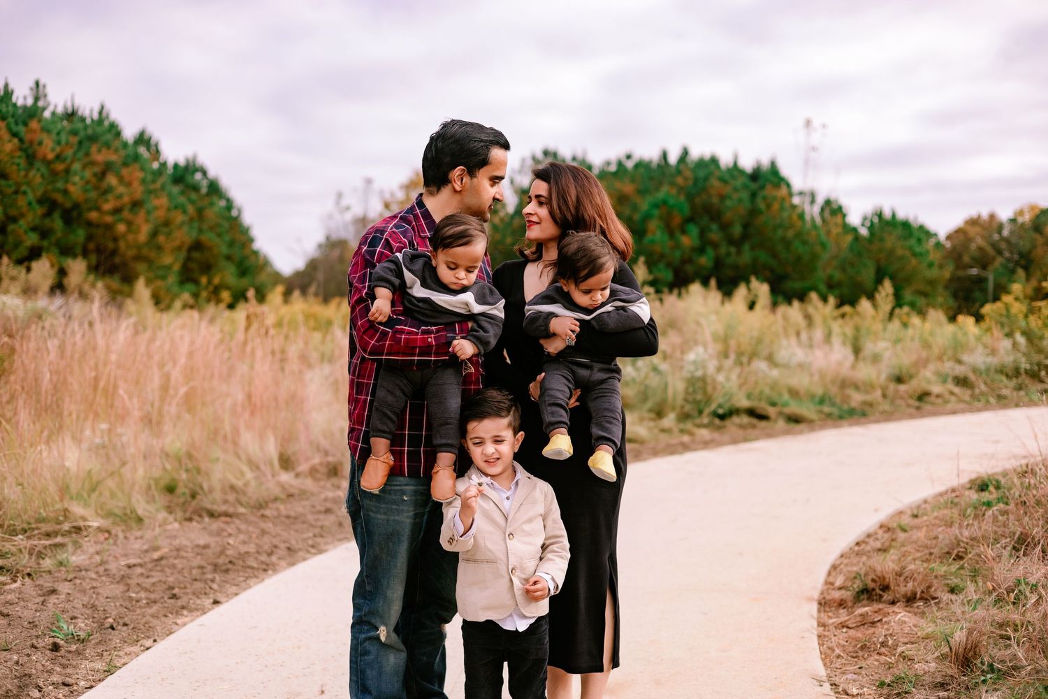 Happy family of five embracing on a scenic path surrounded by fall foliage and tall grasses.