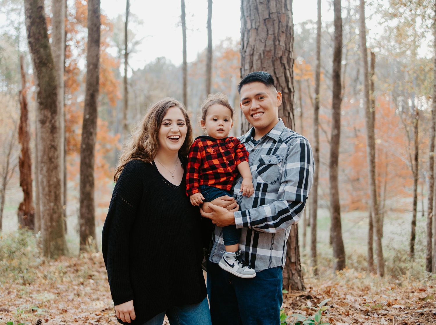 Smiling family of three posing together in an autumn forest with colorful foliage.