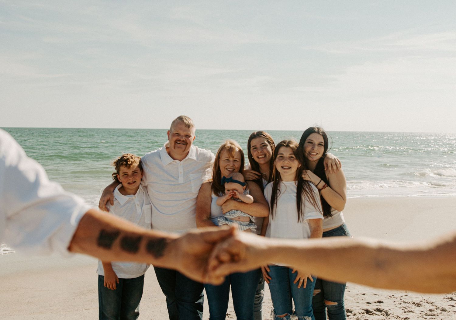 Large family group smiling on a sunny beach with ocean waves in the background.