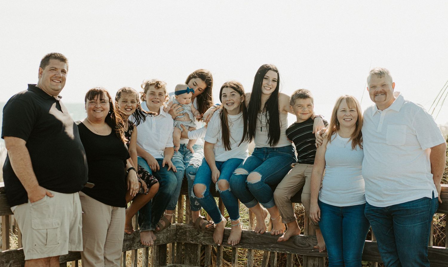 Extended family group portrait taken outdoors near a scenic coastal setting at sunset.