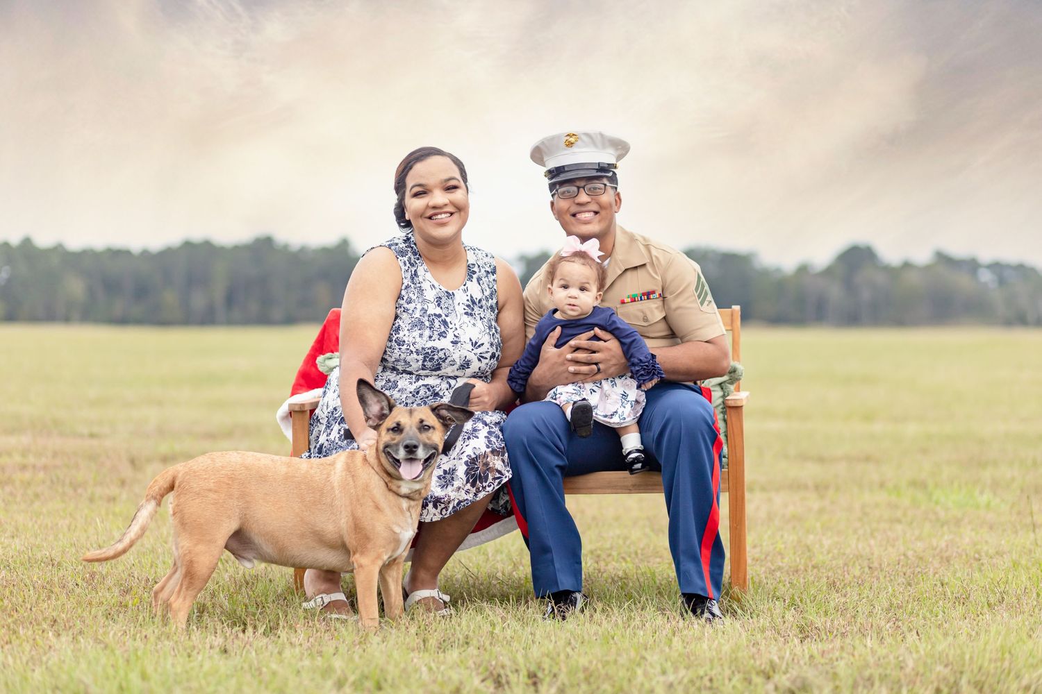 Marine family portrait with wife, baby, and dog sitting outdoors in an open field.