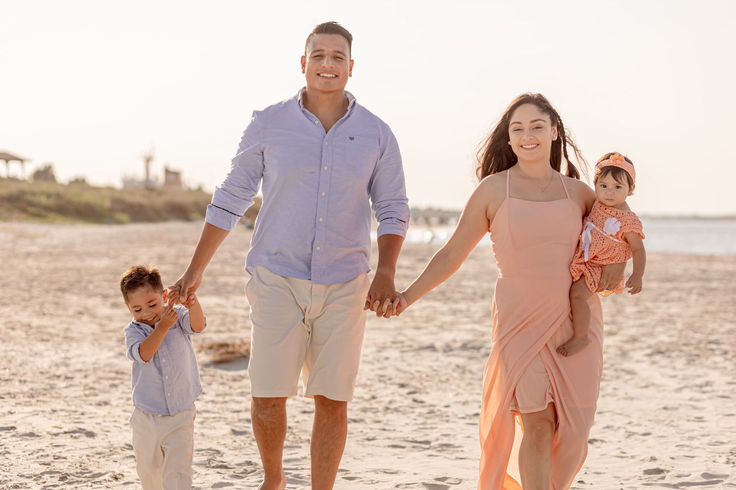 Happy family of four walking hand in hand along a golden sandy beach at sunset.