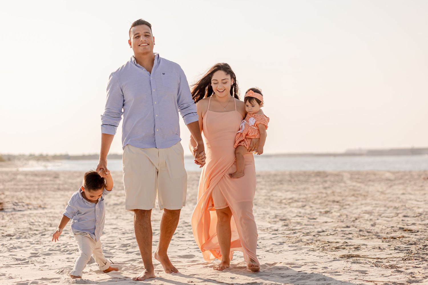 Family of four walking barefoot on a sandy beach during warm golden hour photography.