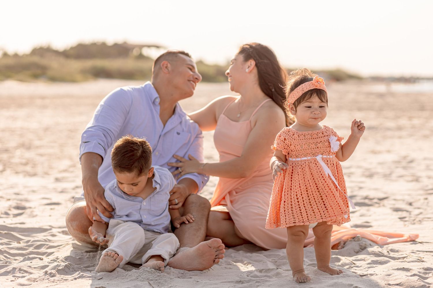 Happy family of four sharing joyful moment together sitting on sandy beach at golden hour.