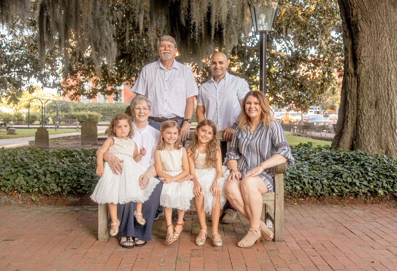 Multi-generational family portrait seated and standing on a brick plaza under Spanish moss-draped trees.