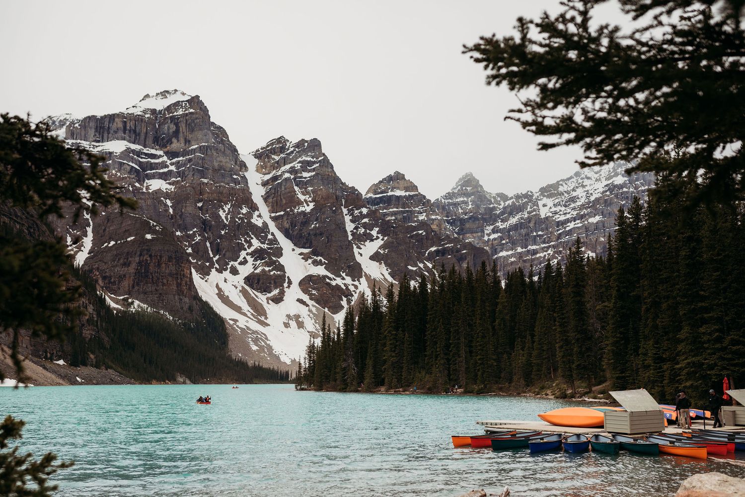 Snow-capped mountain peaks tower over Moraine Lake with canoes lined up along the shore.