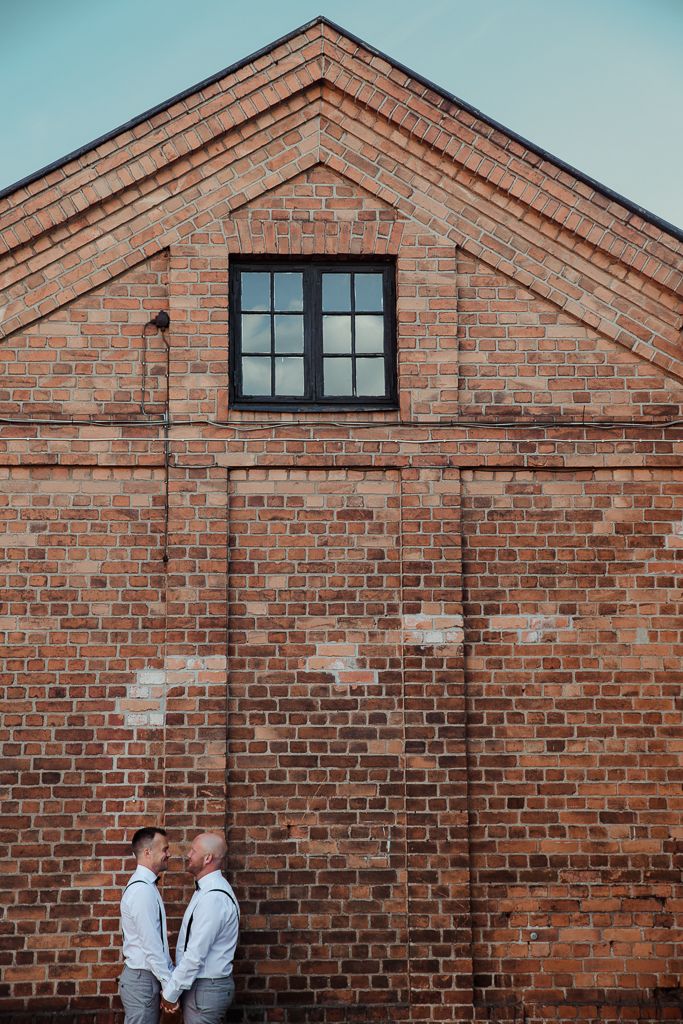 Två brudgummar framför tegelvägg. Bröllopsfotograf i Eskilstuna.
