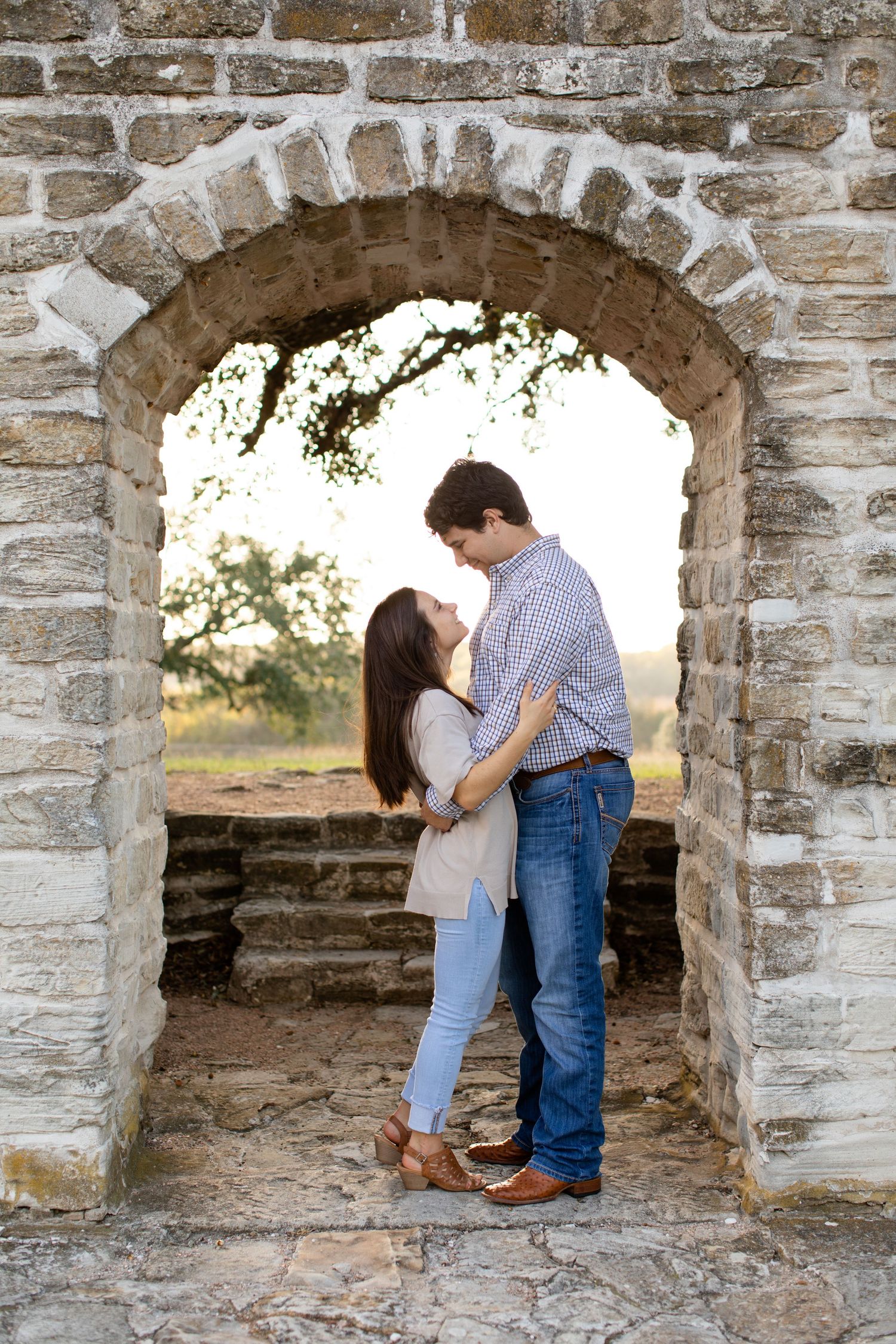 Two people share an intimate moment under an old stone arch.