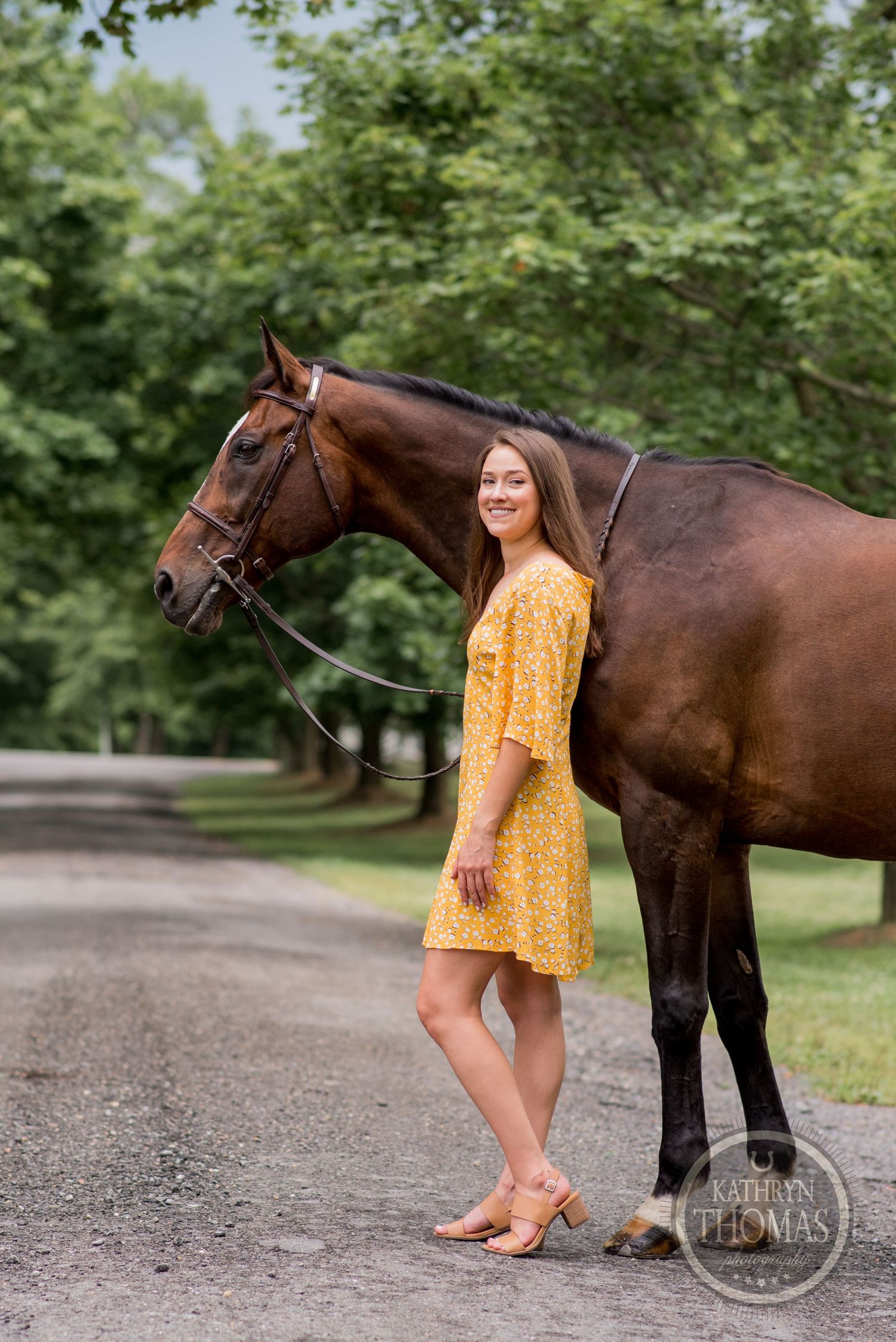A bay horse and companion in a yellow sundress pose together on a shaded path.