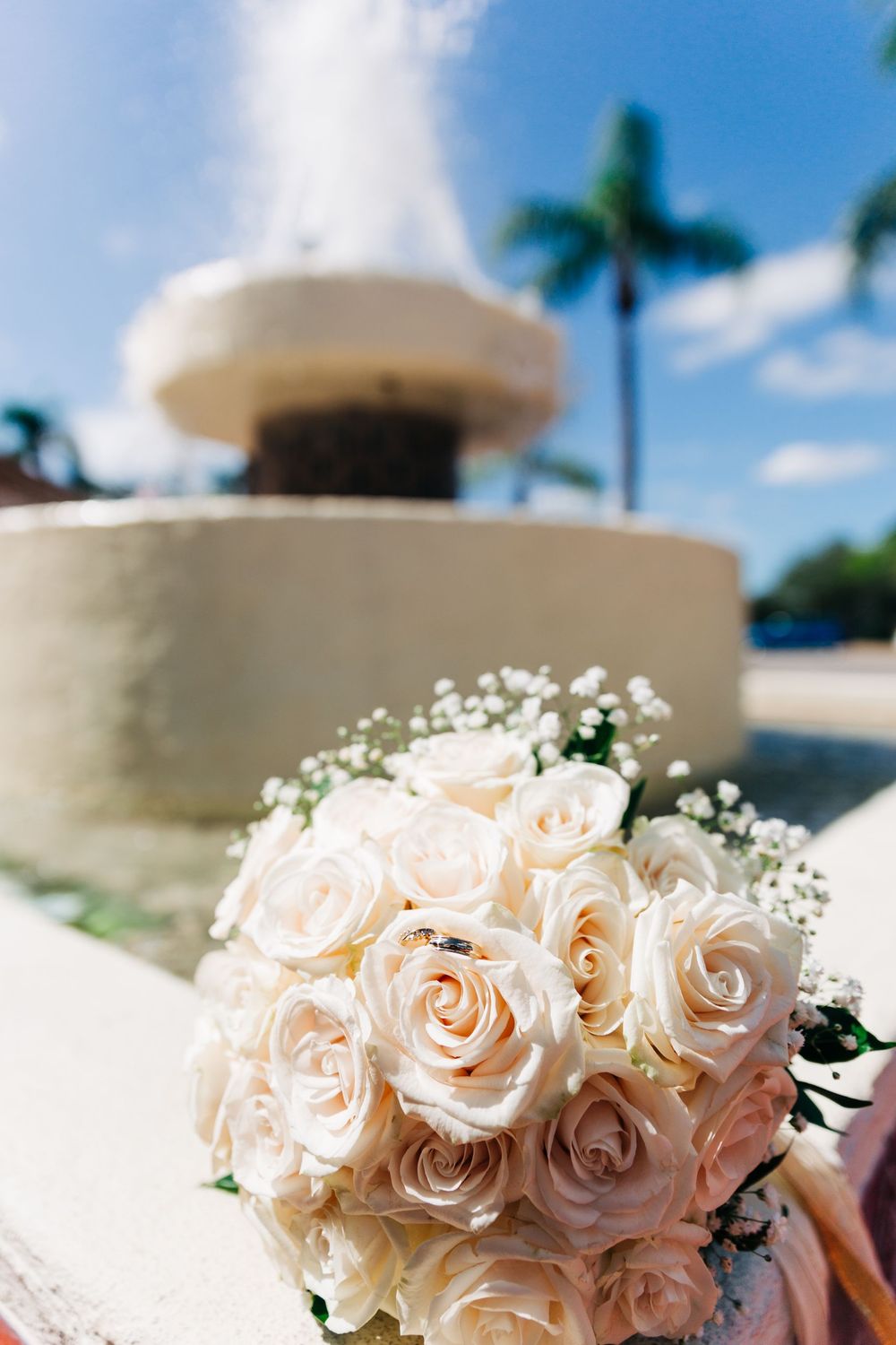White rose wedding bouquet positioned against a fountain and palm trees in tropical setting.