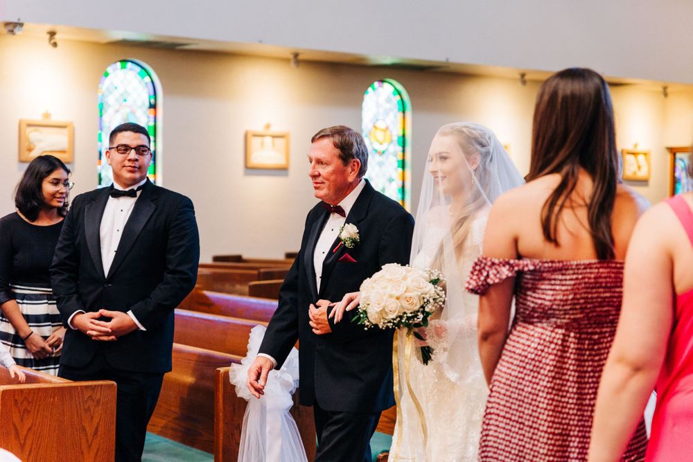 Wedding ceremony taking place in church pews with stained glass windows.