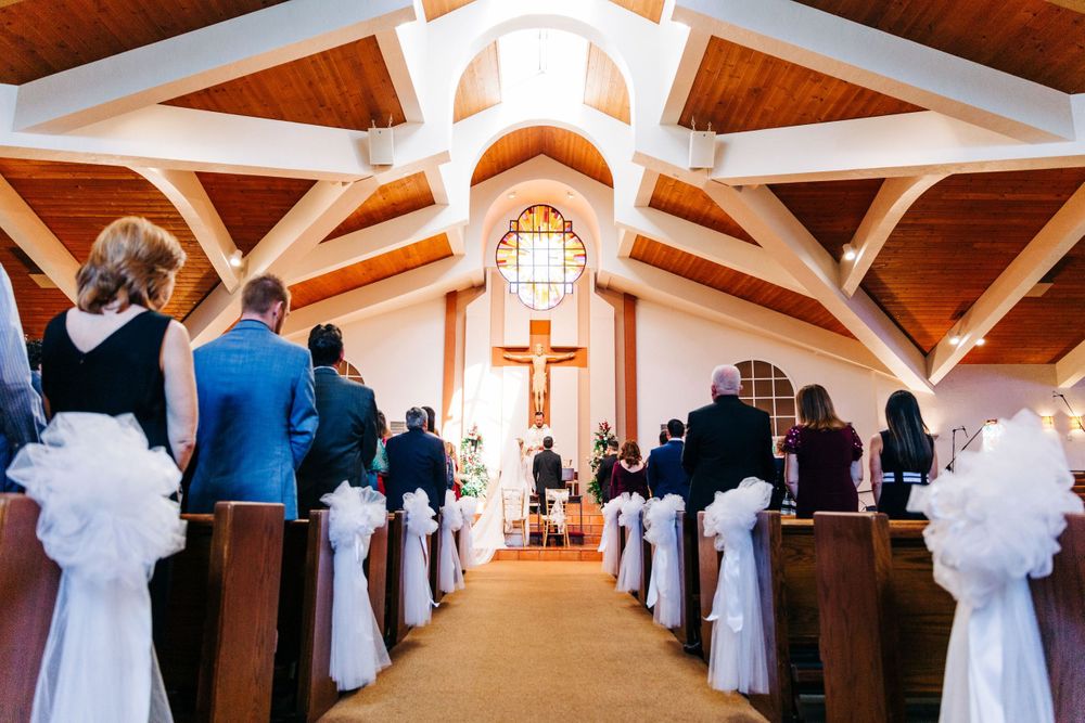 Church wedding ceremony aisle decorated with white bows and cross at altar.