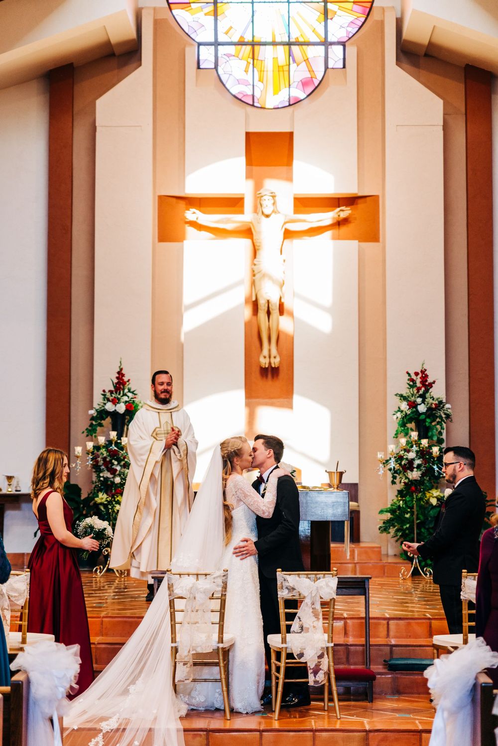 Church wedding ceremony under large crucifix with stained glass windows and Christmas decorations.