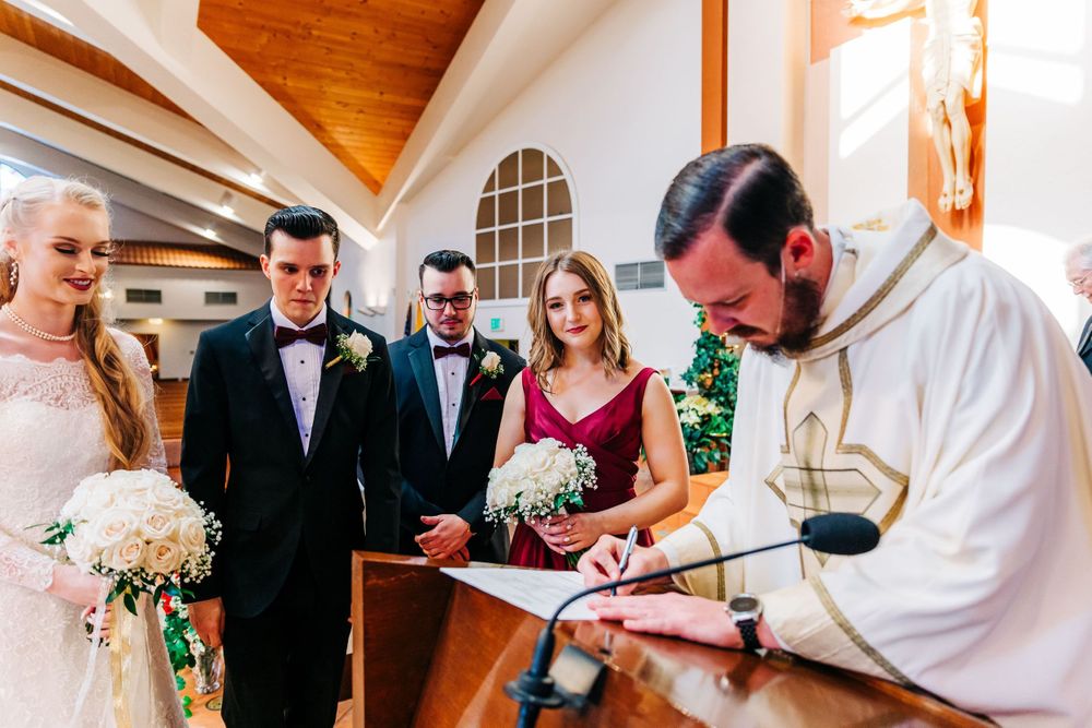 A wedding ceremony moment captured beneath a large crucifix and stained glass window in a church.