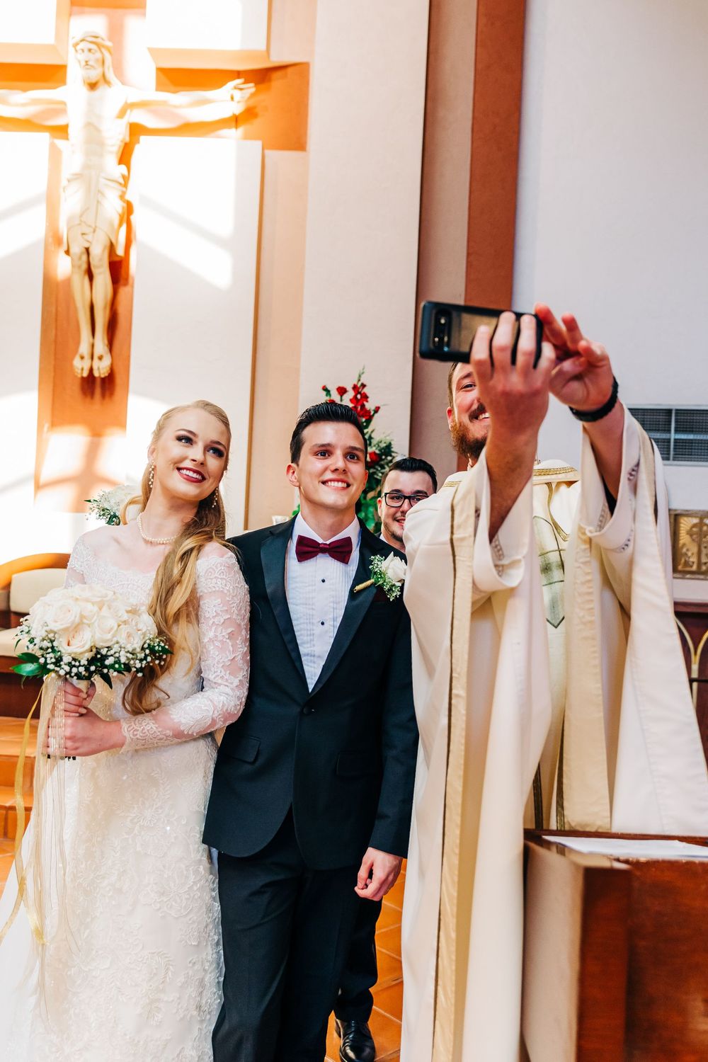 A formal wedding portrait in front of a church altar with a large crucifix and potted plants.