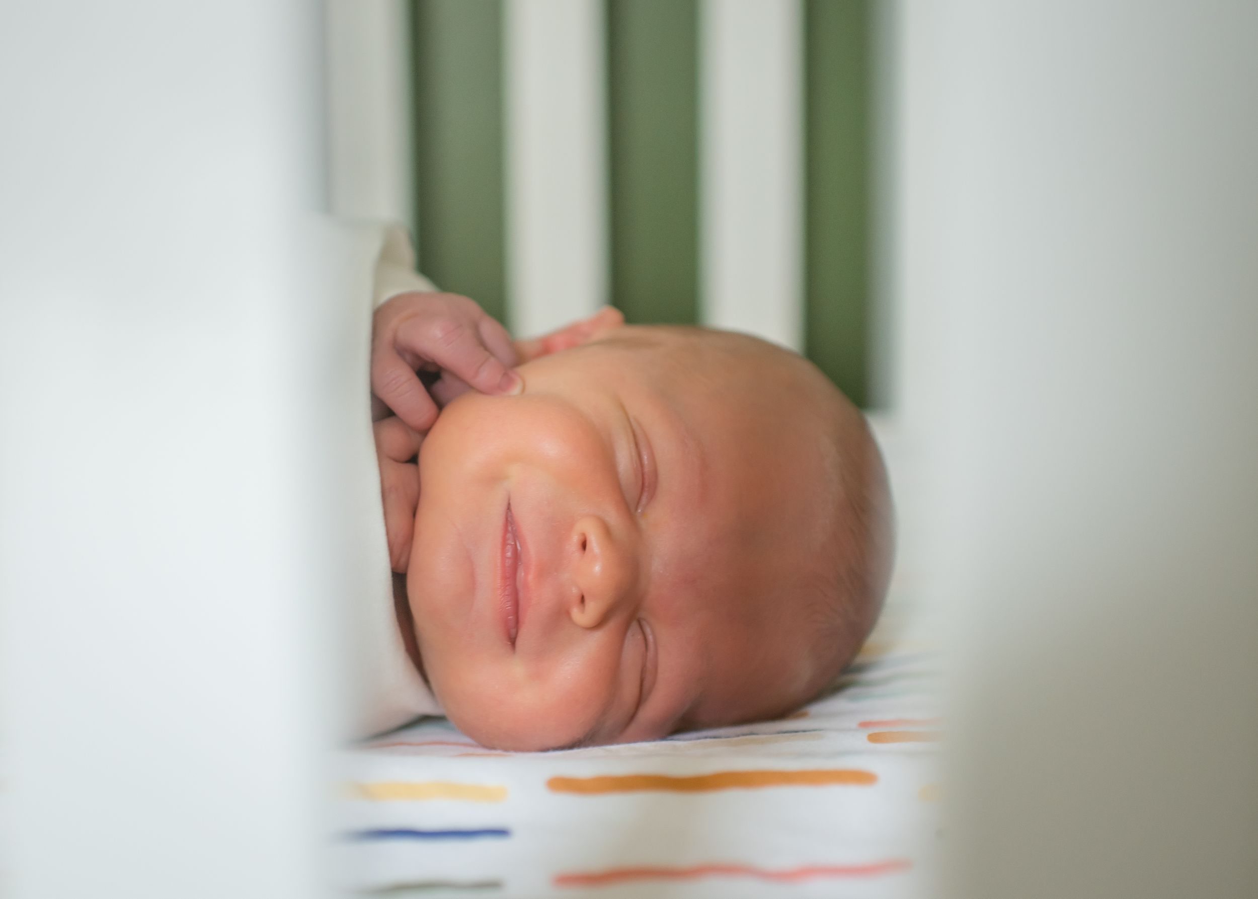 Peaceful sleeping newborn photographed through white crib slats.