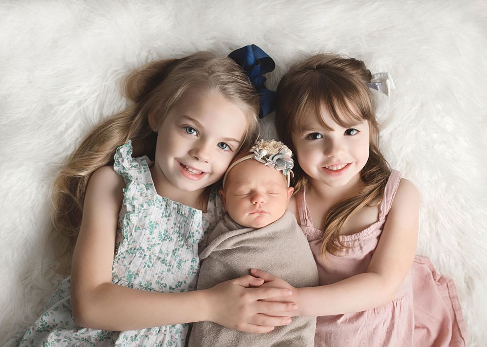 Portrait of three siblings in soft pastel clothing against a white background.