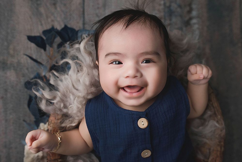 Joyful baby wearing navy blue buttoned outfit against dark backdrop.
