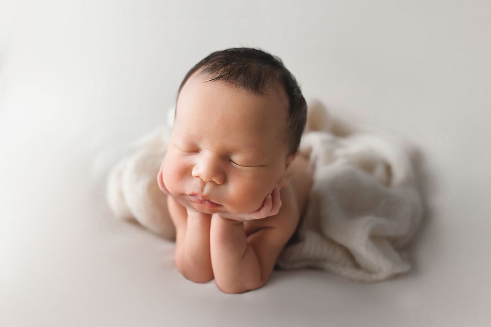 Sleeping newborn baby posed with hands under chin on white background.