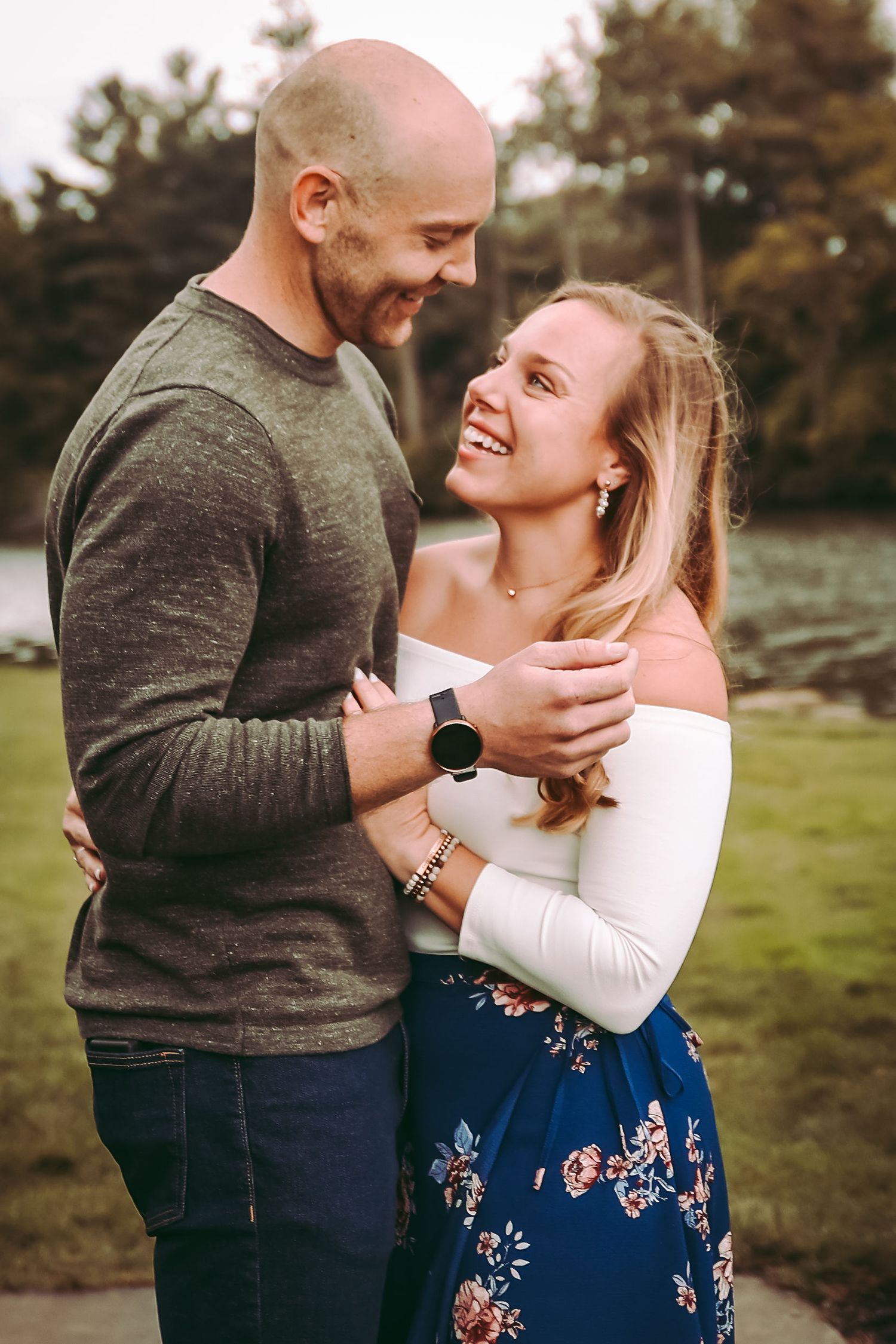 A couple laughing together outdoors wearing casual clothing on a cloudy day.