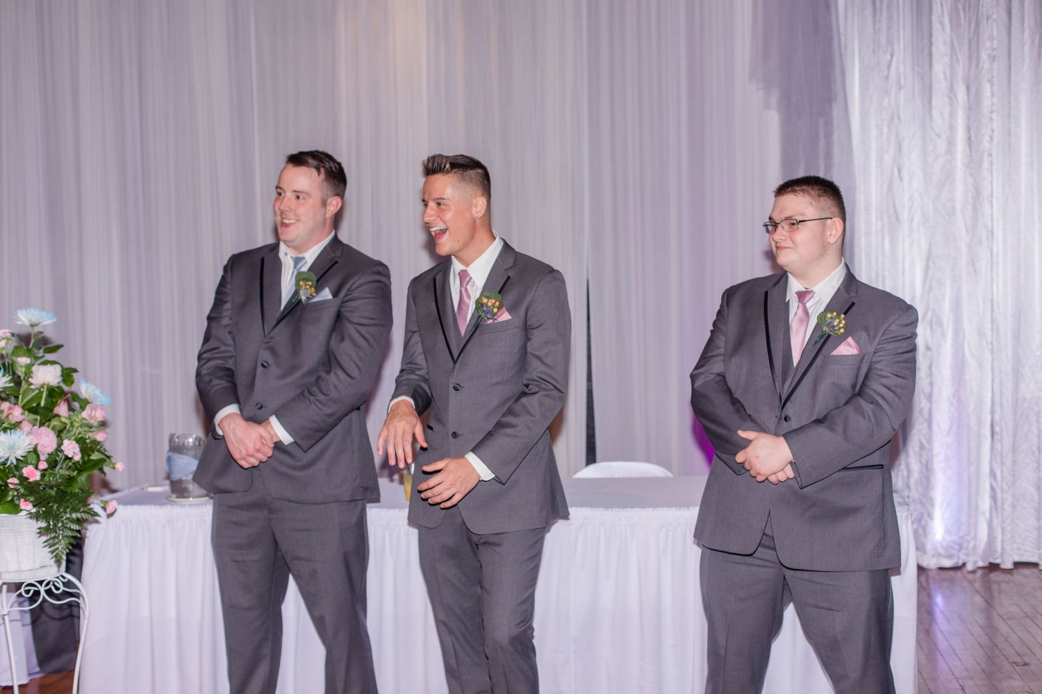 Wedding party members in formal attire pose together against white backdrop with purple lighting.