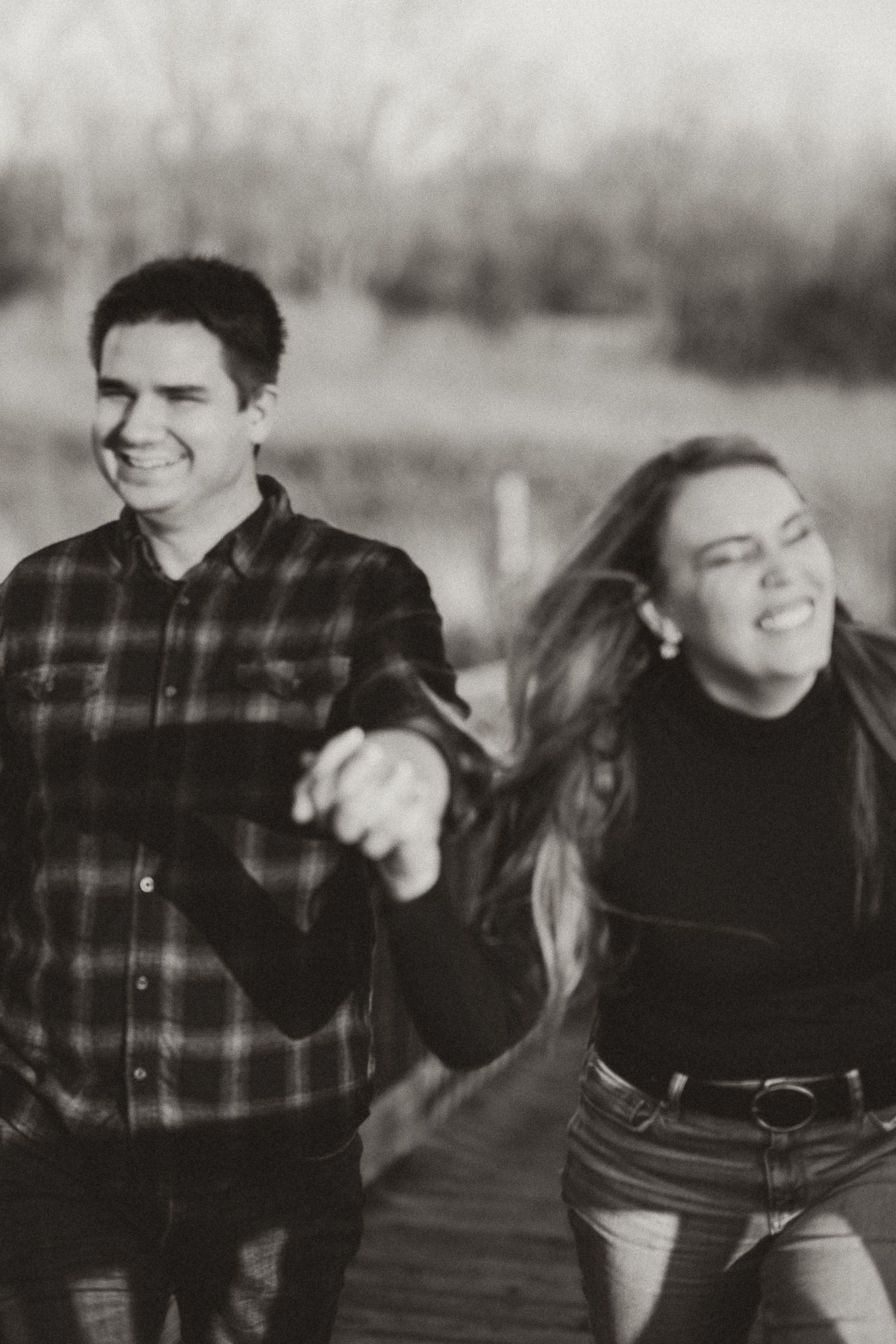A black and white candid photo of a couple laughing together on a wooden boardwalk.