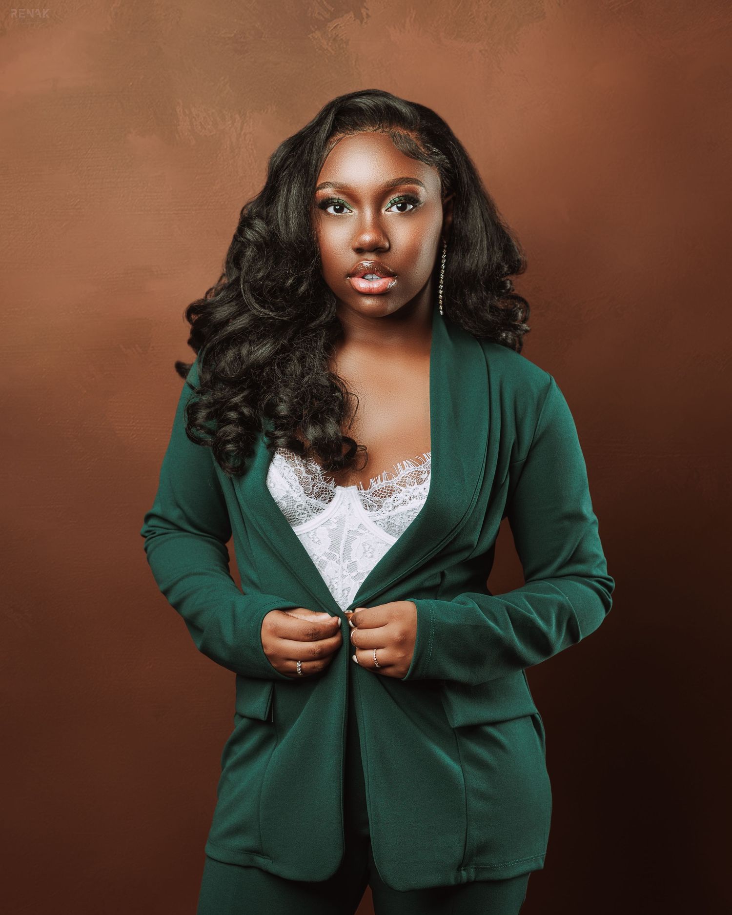 Studio portrait in emerald green blazer and white top against brown background.