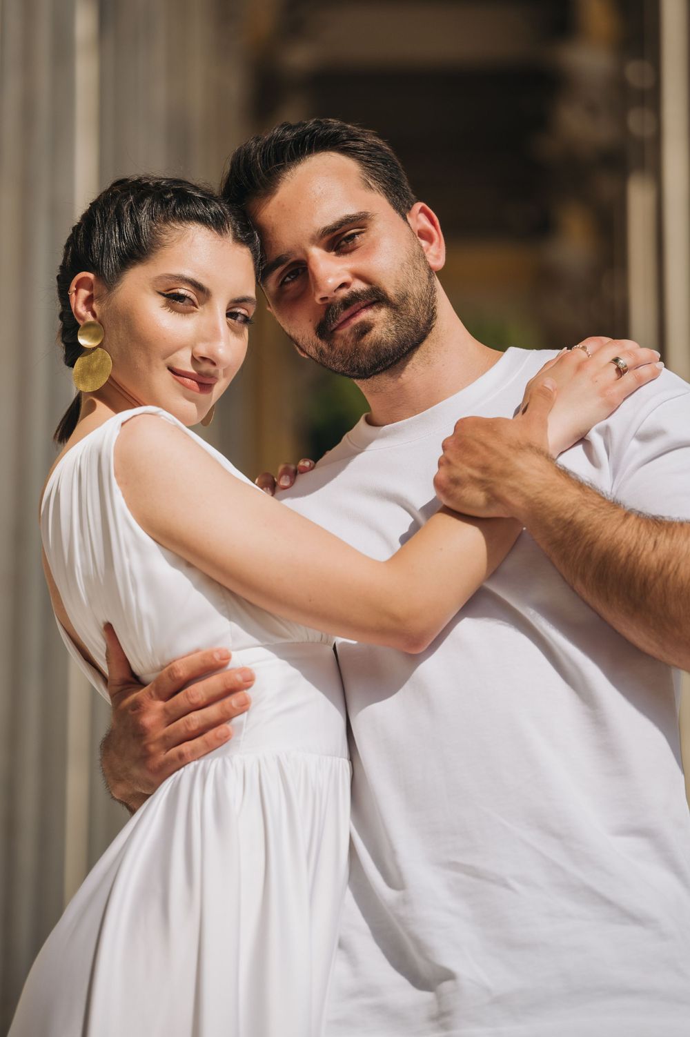 Couple in white dress and casual wear dancing and embracing by classical columns.