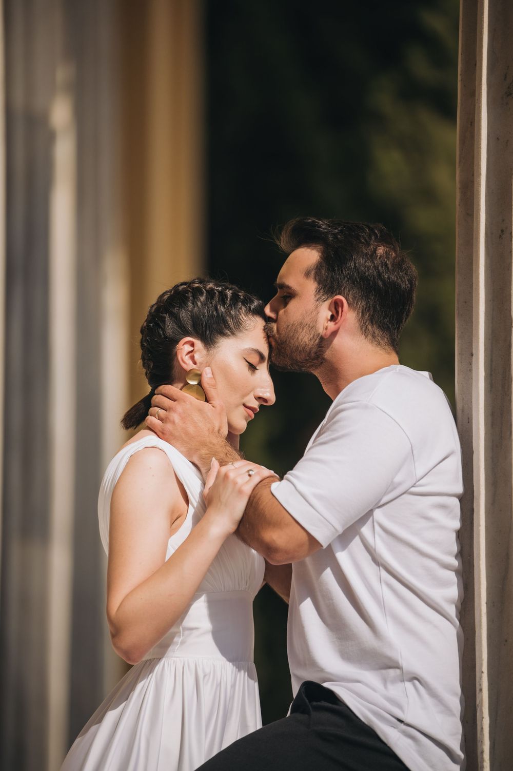 Intimate portrait of couple in white dress and casual wear sharing a romantic moment by columns.
