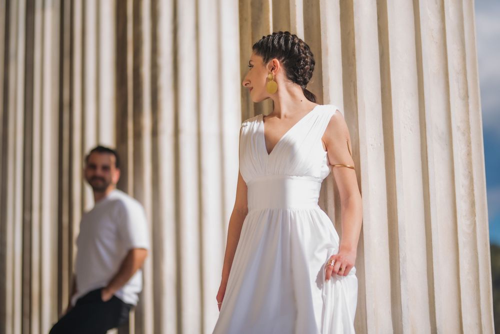 A graceful portrait of two people amid classical stone columns in bright natural lighting.