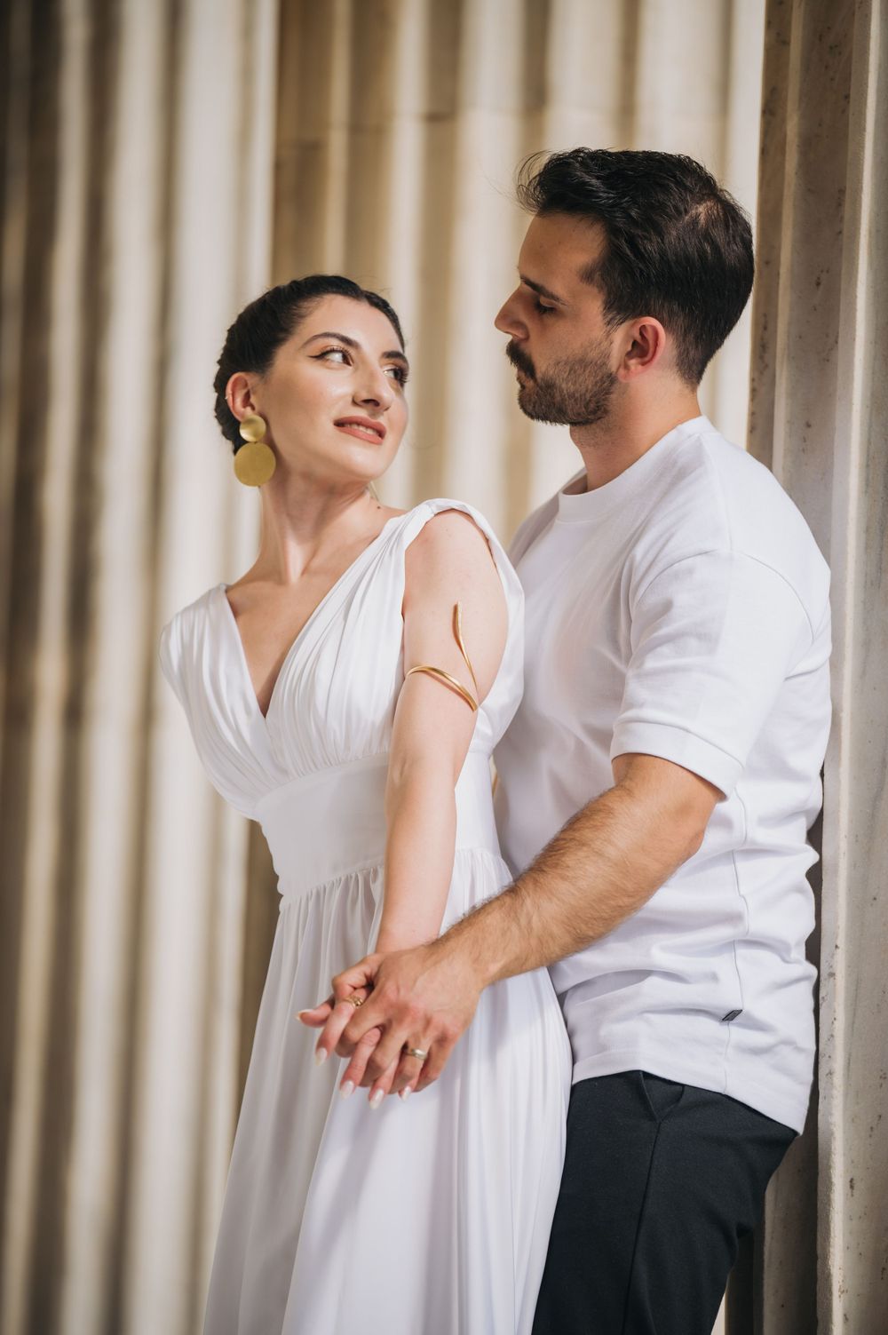 Elegant couple in white dress and casual wear posing by classical columns.