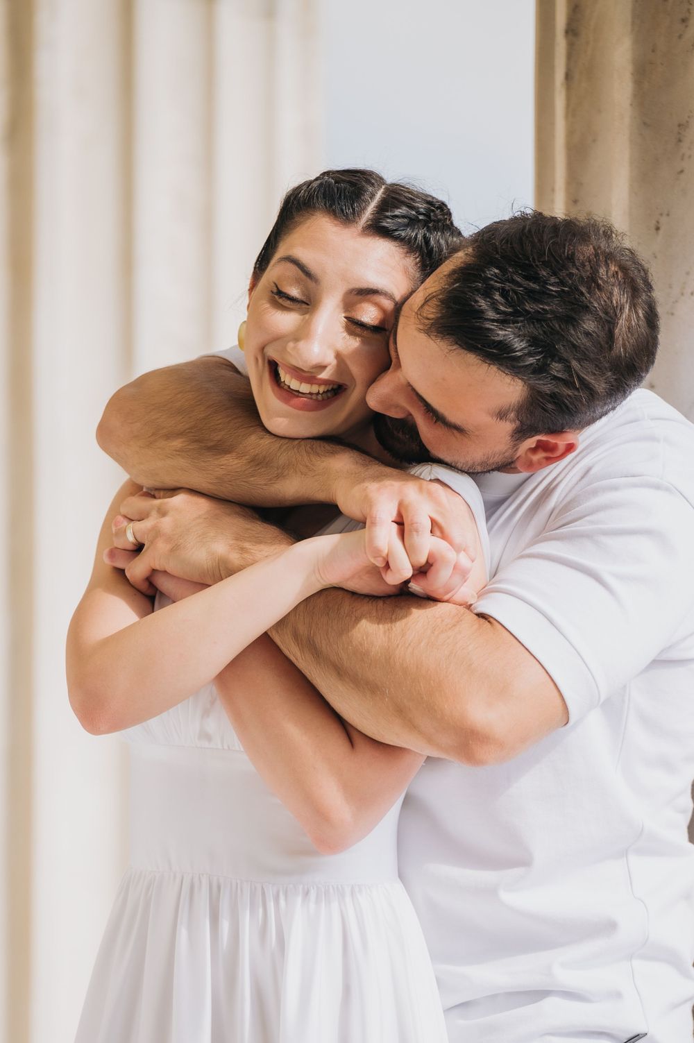 Candid moment of happy couple laughing and embracing in white attire.