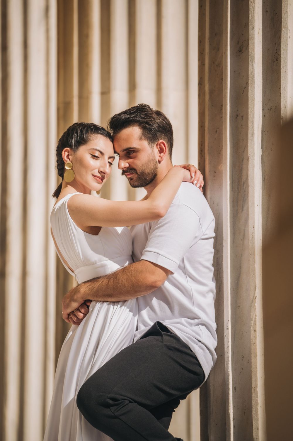 Romantic couple in white and casual attire embracing tenderly against a columned backdrop.