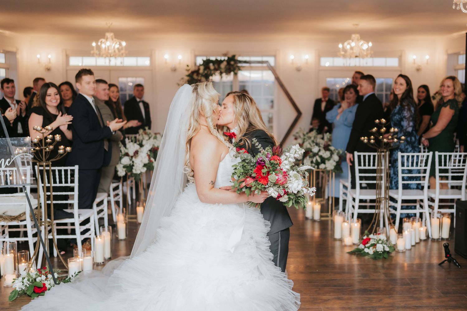 Wedding ceremony in an elegant ballroom with crystal chandeliers and white chiavari chairs.