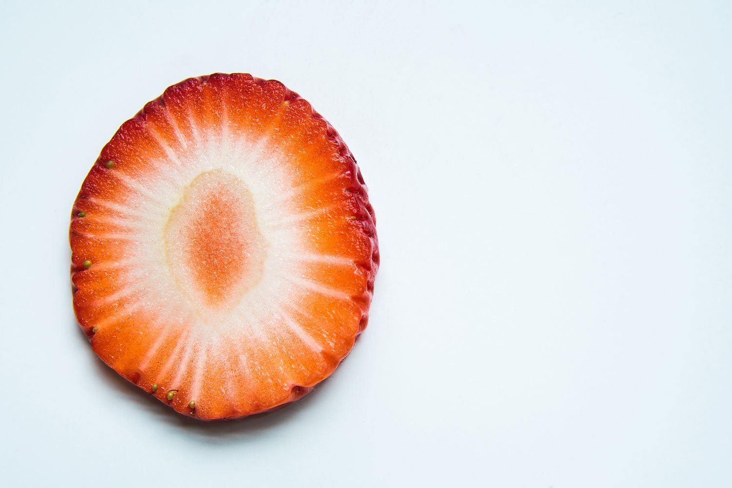 Fresh strawberry slice on white background showing radial pattern and vibrant red color.