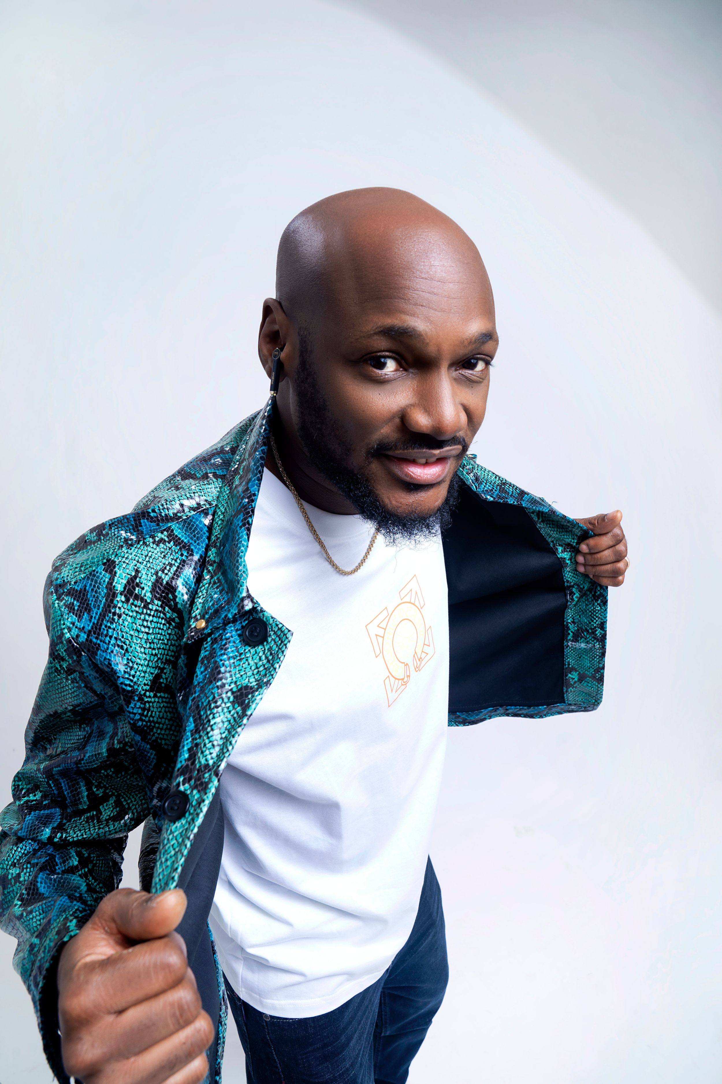 Man in turquoise patterned jacket and white t-shirt poses playfully against white background.