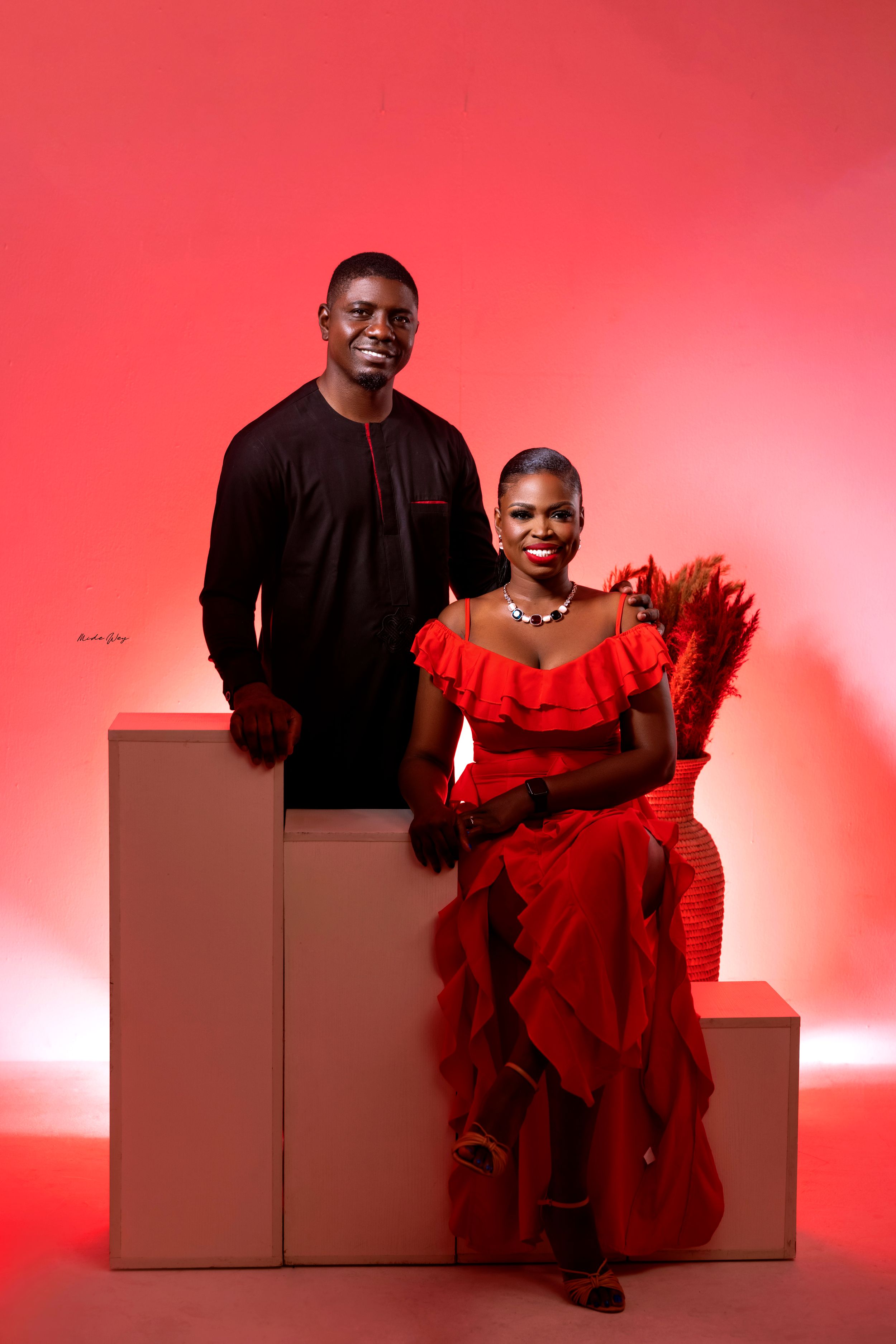 Dramatic studio portrait with red backdrop featuring black and red formal attire.