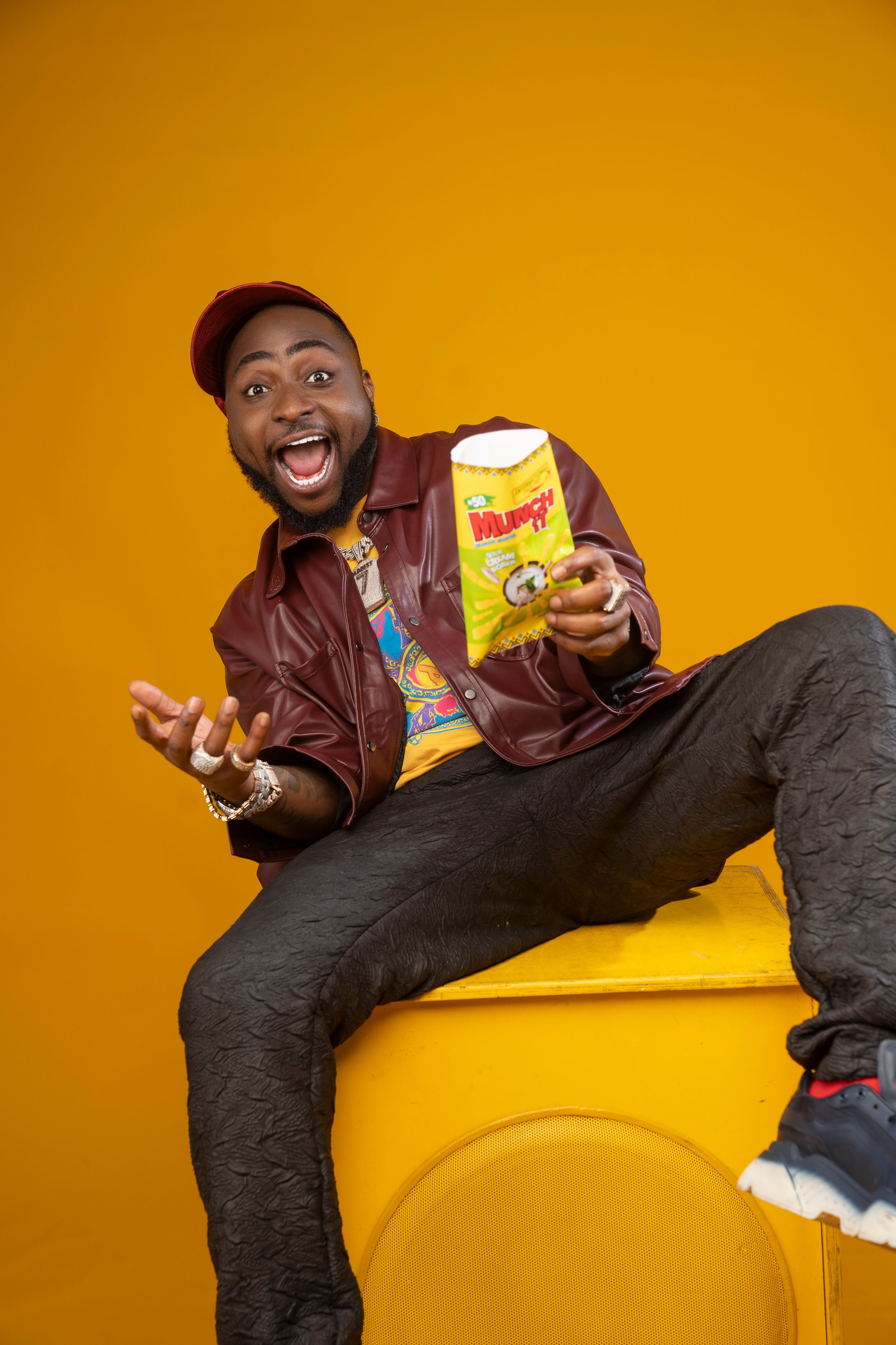 Fun lifestyle photoshoot on yellow couch with snacks and leather jacket.