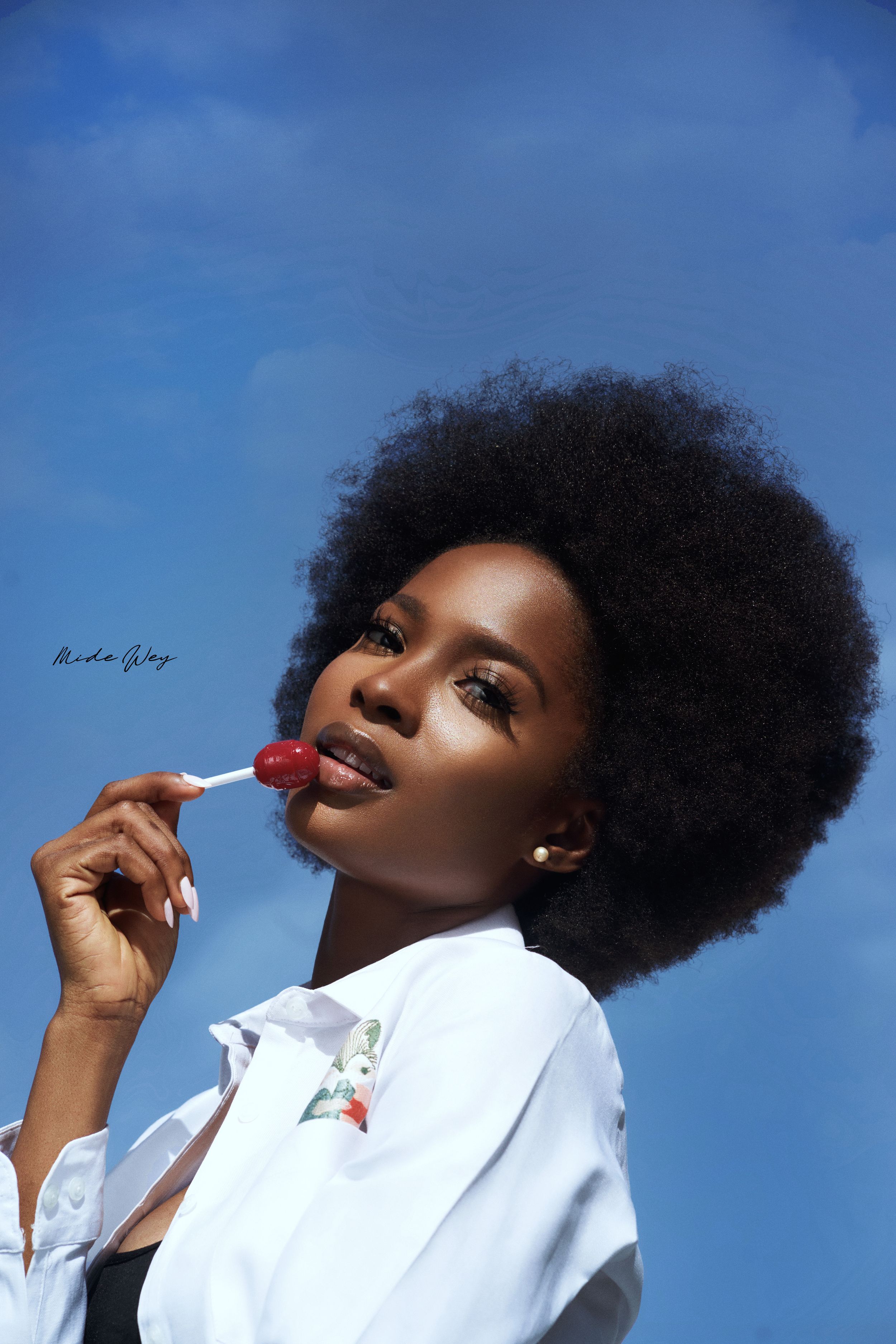 Portrait series against blue sky background showing natural hair and white collared shirt.