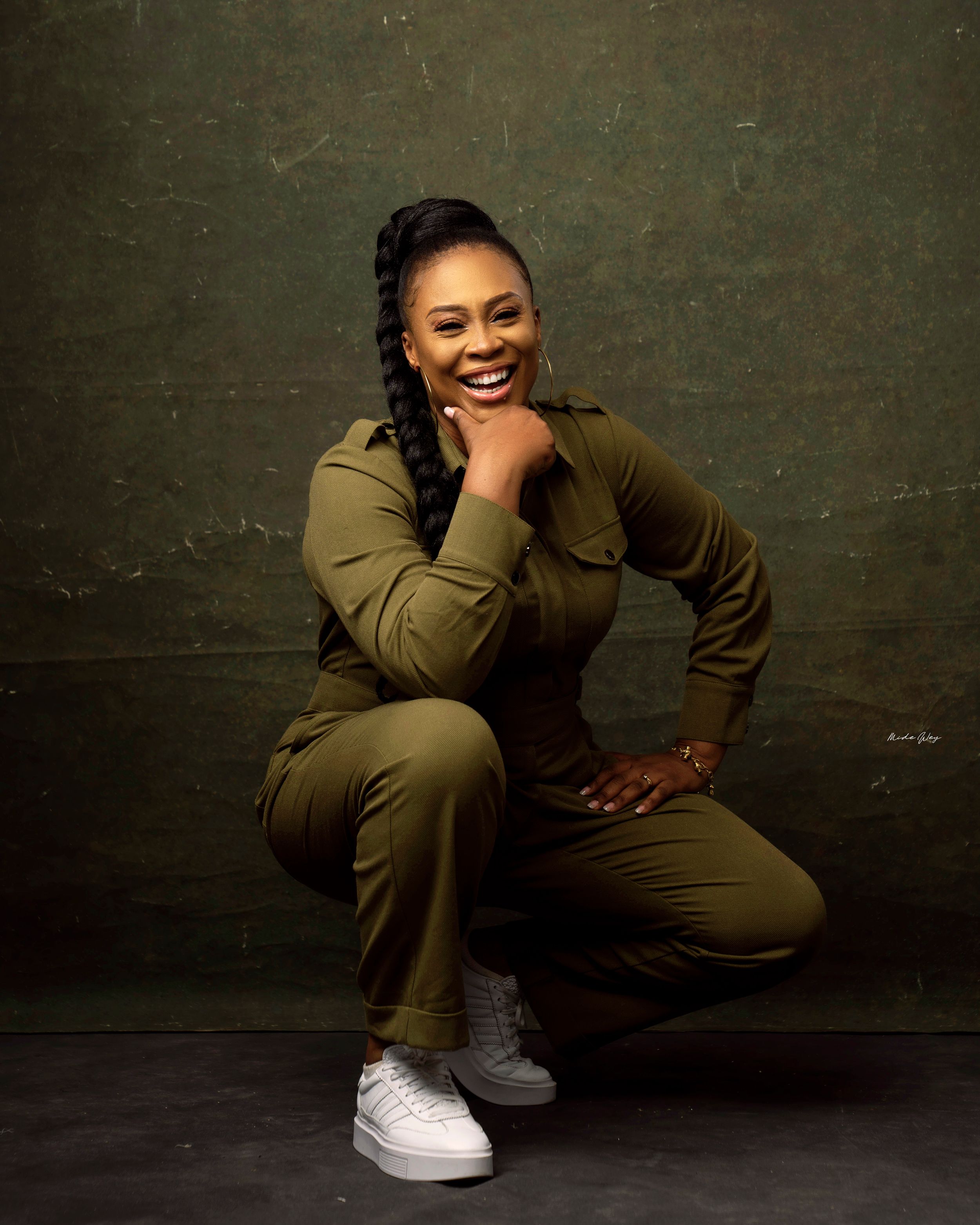 Portrait of a joyful person in olive green jumpsuit and white sneakers against dark background.