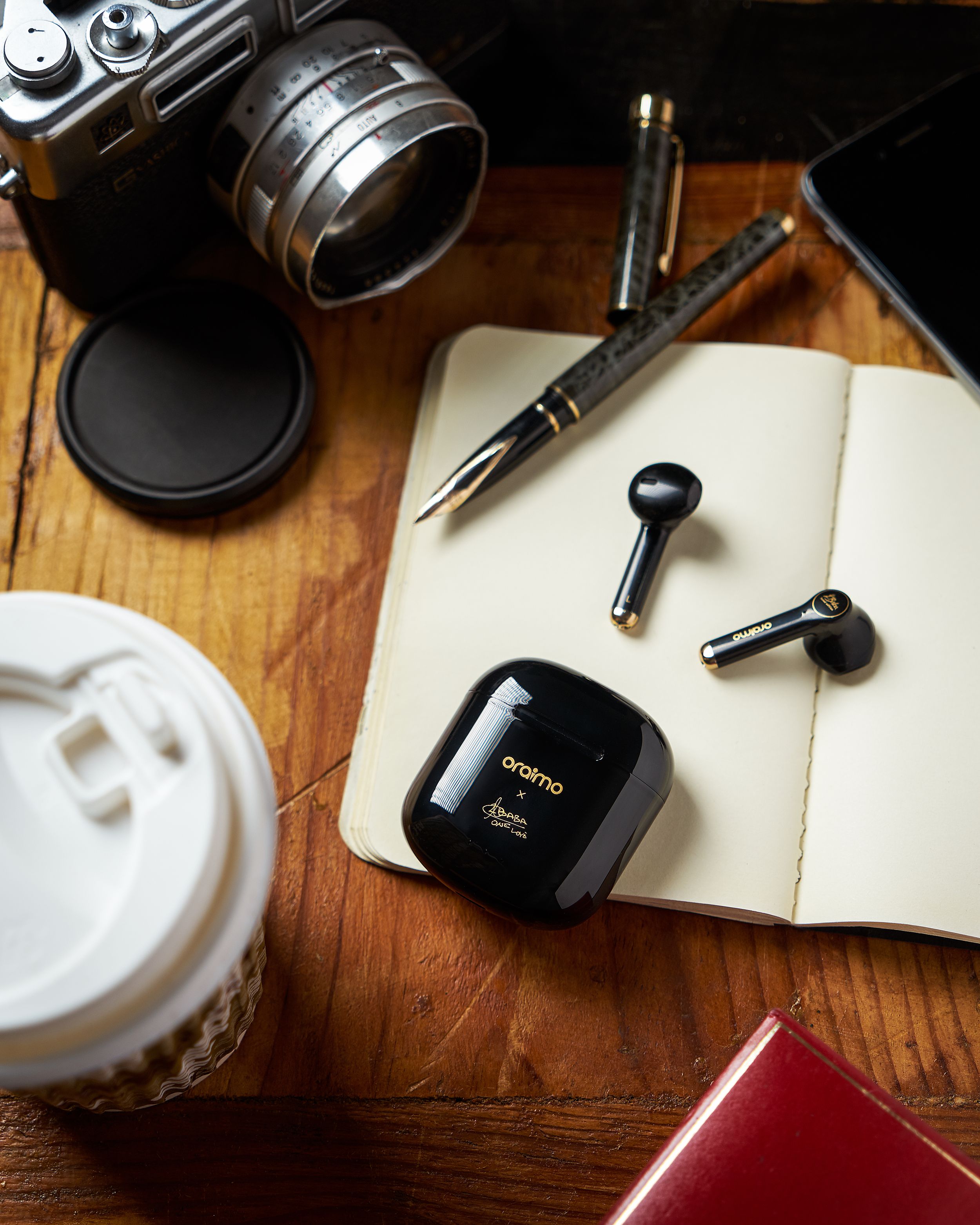 Vintage camera, notebook, earbuds and coffee cup arranged on wooden surface.