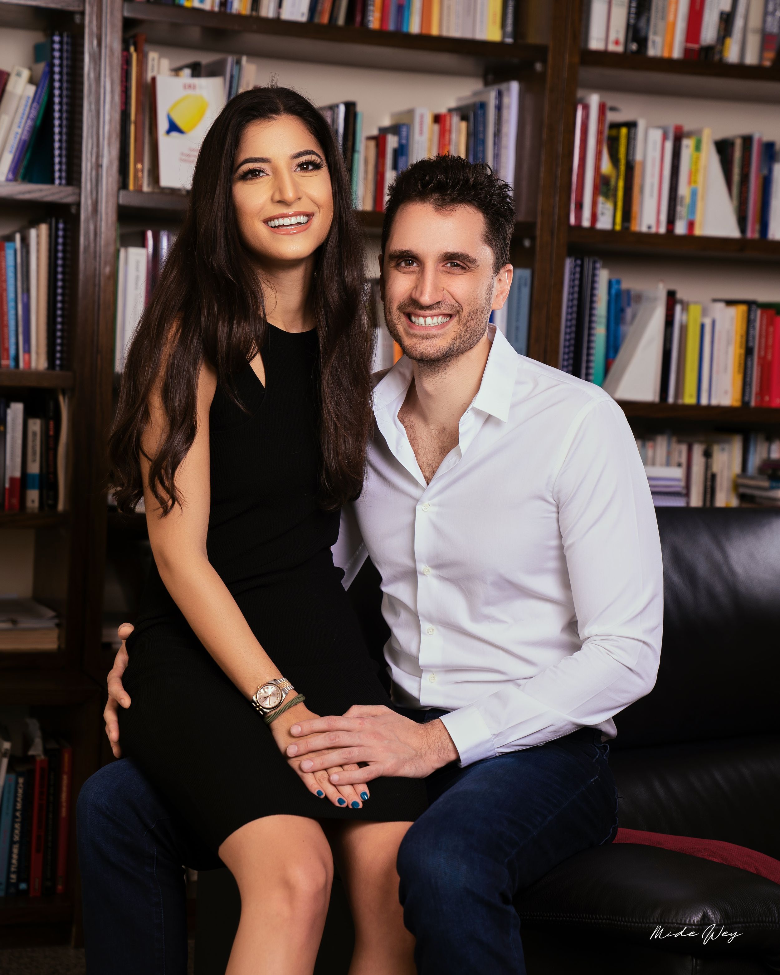 Couple sitting together on leather couch with library bookshelf background.