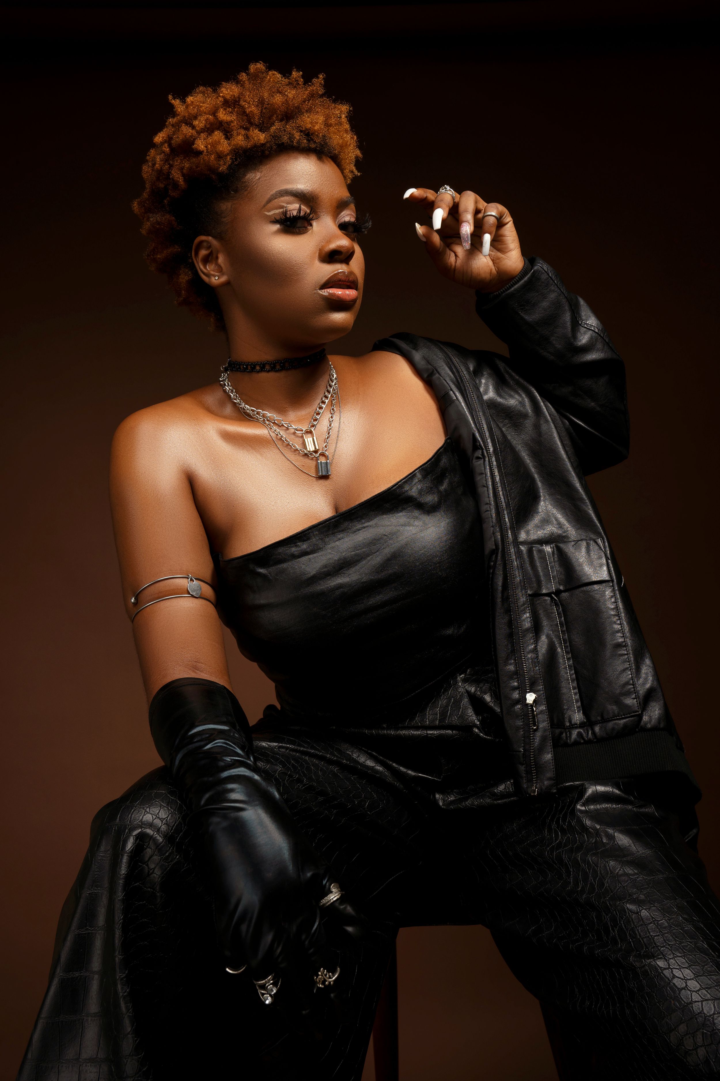 Fashion portrait with leather jacket, gloves and statement necklace against dark backdrop.