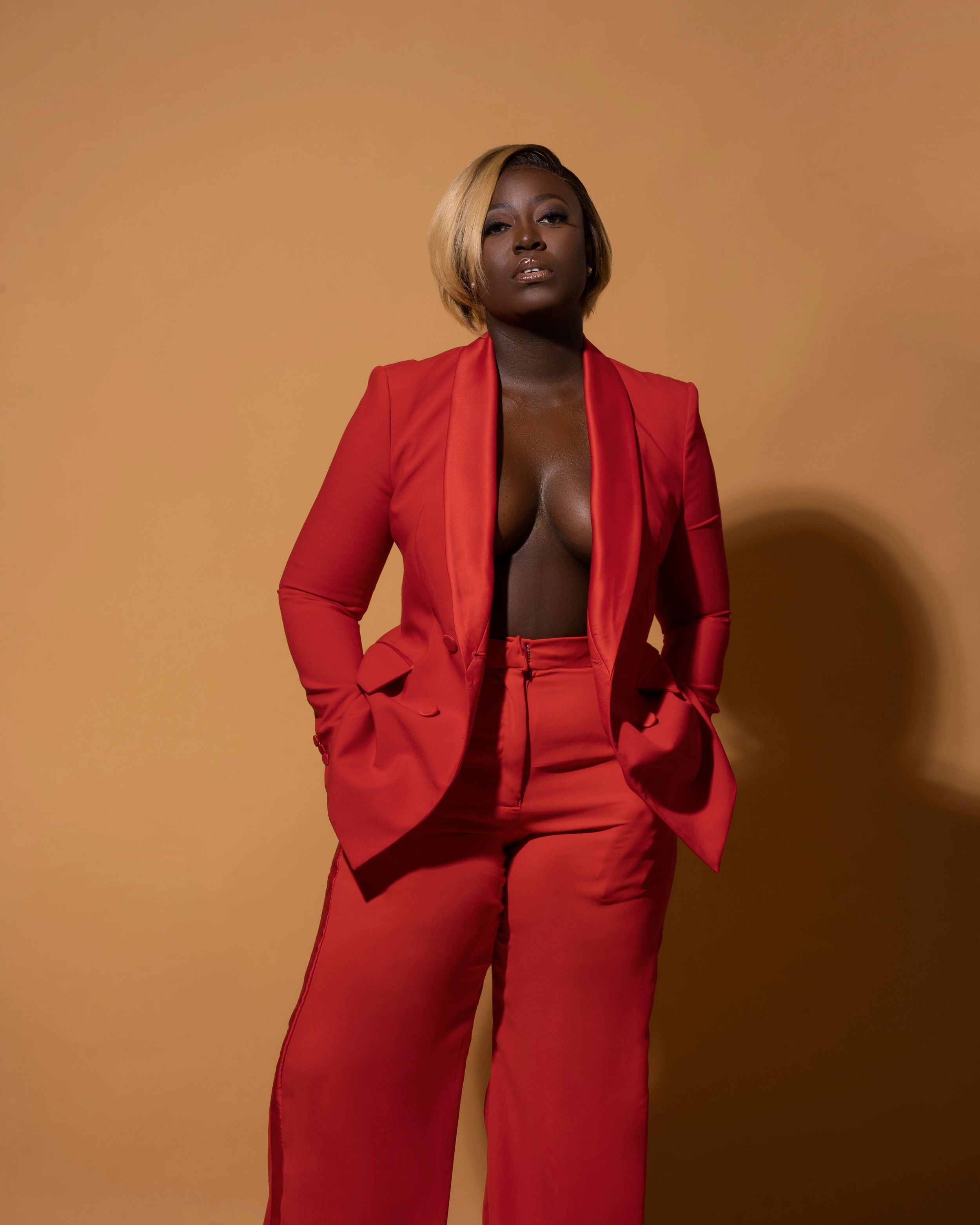 Fashion portrait in bold red power suit against warm brown background.